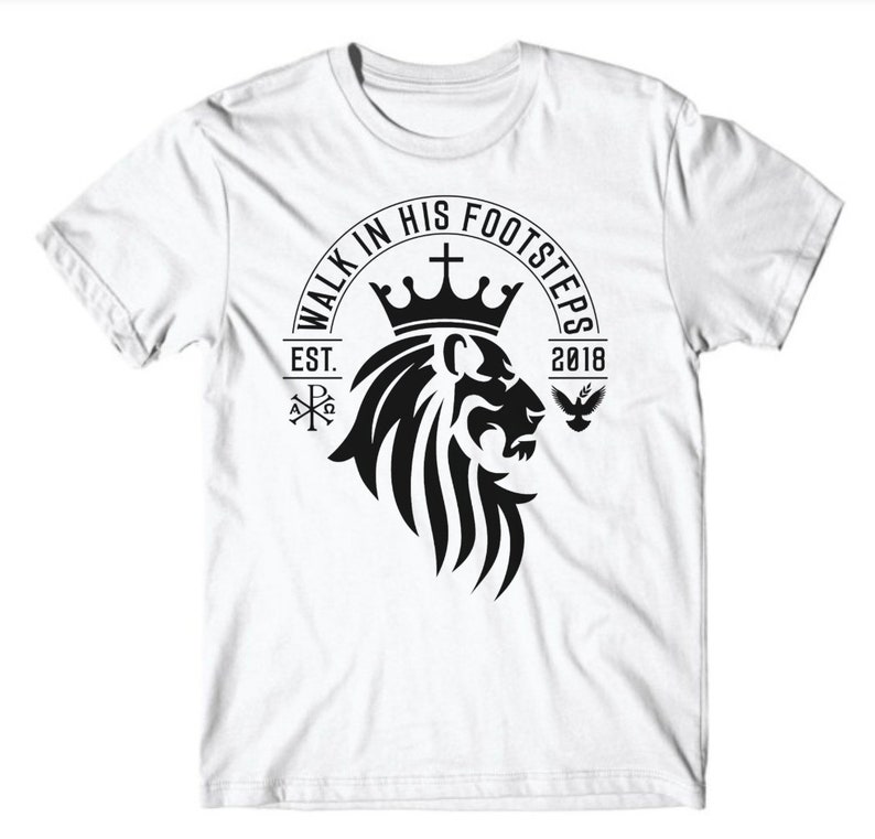 May include: White t-shirt with a black graphic design of a lion's head wearing a crown. The graphic also includes the text "Walk in His Footsteps", "Est. 2018", a cross, and a dove.