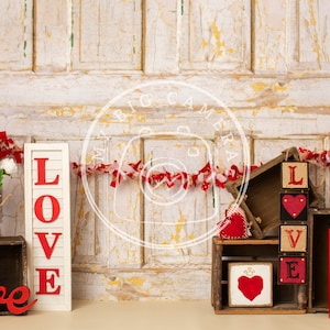 May include: A rustic Valentine's Day decor scene with a whitewashed wooden background.  The scene includes a red and white fabric garland, a red heart with the text "xoxo", a red wooden "love" sign, a wooden sign with the letters "LOVE" in red, and a wooden block sign with the letters "LOVE" in red.