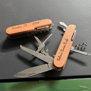 May include: Two wooden handled pocket knives with engraved text. The top knife has the text "Houston TX 2024" engraved on the handle. The bottom knife has the text "Selina's Swiss Knife" engraved on the handle.