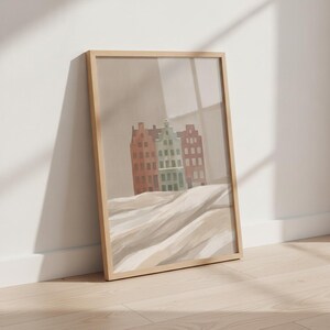 Peut inclure: Une impression d'art mural verticale encadrée représentant une illustration stylisée de trois bâtiments étroits dans des tons sourds de terre cuite et de vert sauge, sur un fond beige neutre avec un premier plan texturé et ondulé en crème et beige.