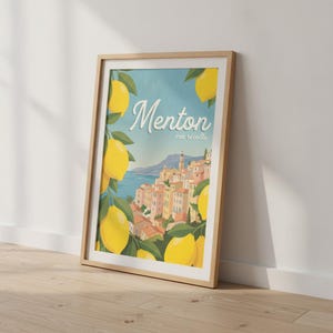 Op de afbeelding: Een ingelijste verticale kunstdruk met een kuststadje en de tekst Menton ma récolte. De illustratie toont heldergele citroenen aan groene takken op de voorgrond, uitkijkend over een mediterrane stad met gebouwen in pasteltinten.