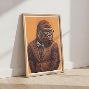 Peut inclure: Une impression d'art encadrée représentant un gorille brun portant un blazer beige, un nœud papillon à motifs et des lunettes à monture noire. Le gorille est placé sur un fond orange uni, dans un style portrait avec un cadre en bois clair.