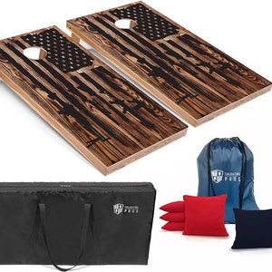 May include: Two wooden cornhole boards with an American flag design and black silhouettes of guns. The boards are set up for a game of cornhole. The set includes a black carrying bag, blue and red bean bags, and a blue drawstring bag with the logo "Tailgating Pros".