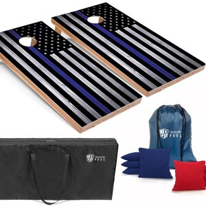 May include: A set of two wooden cornhole boards with a thin blue line American flag design. The set includes a black carrying case, a blue drawstring bag, and eight bean bags, four red and four blue.