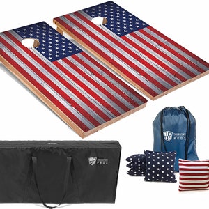 May include: A set of two regulation-sized cornhole boards with an American flag design. The boards are made of wood and have a distressed wood look. The set includes eight bean bags, a carrying case, and a drawstring bag. The bean bags are red, white, and blue with a star pattern.
