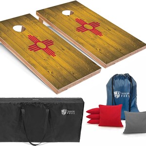 May include: A set of two wooden cornhole boards with a New Mexico flag design. The boards are yellow with red and white accents. The set includes a black carrying bag, a blue drawstring bag, and eight bean bags: four red and four gray.