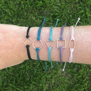 May include: Six colorful friendship bracelets with gold geometric charms. The charms include a square, circle, triangle, square, oval, and diamond.
