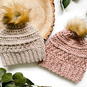May include: Two crocheted hats with faux fur pom poms. One hat is beige and the other is pink.