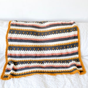 May include: A striped crocheted throw blanket with a textured pattern in shades of gray, white, mustard yellow, and pink.