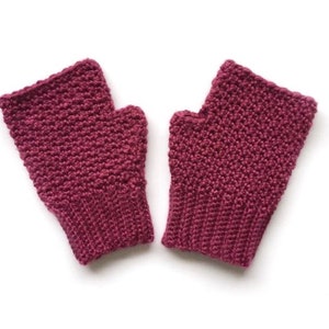 May include: A pair of knitted fingerless gloves in a deep burgundy colour. The gloves have a textured stitch pattern and a ribbed cuff.