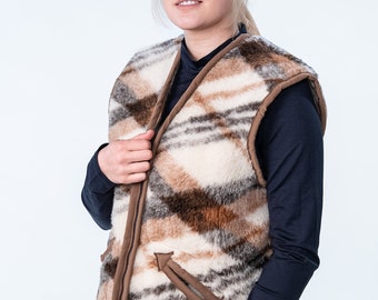 May include: A brown, white, and black patterned vest with a zipper closure and a brown pocket on the front. The vest is made of a soft, fuzzy material.