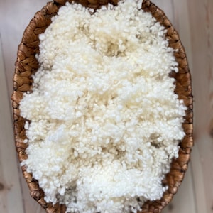 May include: A white fluffy material in a brown wicker basket. The material is perfect for newborn photography props.