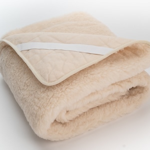 May include: A cream-colored sheepskin mattress topper with a white quilted lining and a white fabric strap.