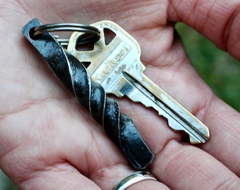 May include: A hand holding a key with a black metal key chain. The key has a silver finish and the text "Weiser" is visible on the key.