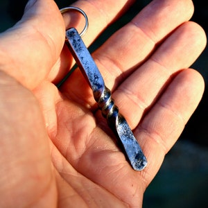 May include: A twisted metal keychain with a silver finish. The keychain is attached to a silver ring.