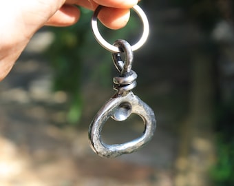 Può includere: Apribottiglie in metallo forgiato a mano con portachiavi. L'apribottiglie ha un aspetto strutturato e rustico e un anello per un facile fissaggio. Il metallo è di colore argento e il design è semplice ma funzionale. Un oggetto unico e fatto a mano.
