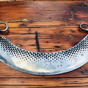 May include: A silver cheese knife with a curved blade and two twisted handles. The blade has a textured surface.