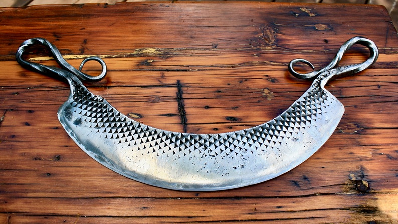 May include: A silver cheese knife with a curved blade and two twisted handles. The blade has a textured surface.