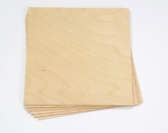 May include: A stack of unfinished, light-colored plywood boards. The wood grain is visible, and the boards are rectangular. The boards are stacked on a white surface.
