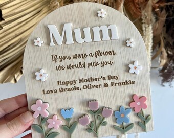 May include: Wooden sign with the word "Mum" in white letters. The sign has a floral design with pink, blue, and green flowers. The text reads "If you were a flower, we would pick you. Happy Mother's Day. Love Gracie, Oliver & Frankie."