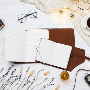 May include: A flat lay of a white wooden surface with two open notebooks, a pen, a jar of honey, a cup of tea, a knitted blanket, string lights, dried lavender, and a small glass bottle with a cork.