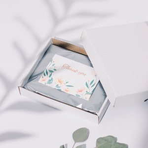 May include: A white gift box with a floral thank you card inside. The box is open and the card is visible. The card has a floral design and the words "Thank you" in red.