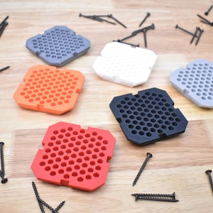 May include: Five hexagonal shaped trays with a honeycomb pattern in different colors: orange, red, black, white, and gray. The trays are on a wooden surface with black screws scattered around them.