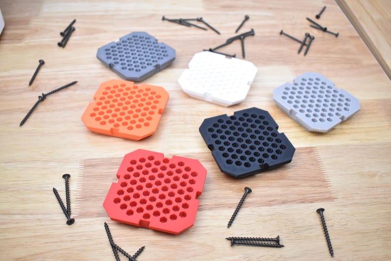 May include: Five hexagonal shaped trays with a honeycomb pattern in different colors: orange, red, black, white, and gray. The trays are on a wooden surface with black screws scattered around them.
