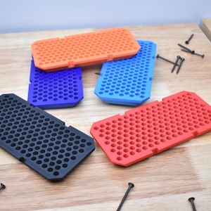 May include: Four different colored plastic trays with a honeycomb pattern. The trays are black, red, blue, and orange. The trays are on a wooden surface.