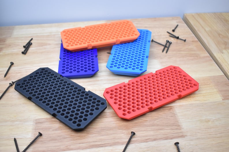 May include: Four different colored plastic trays with a honeycomb pattern. The trays are black, red, blue, and orange. The trays are on a wooden surface.