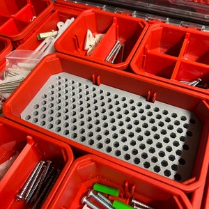 May include: A red plastic storage box with multiple compartments. The box contains a variety of small hardware items, including screws, nails, and plastic anchors. The bottom compartment has a gray honeycomb-shaped insert.