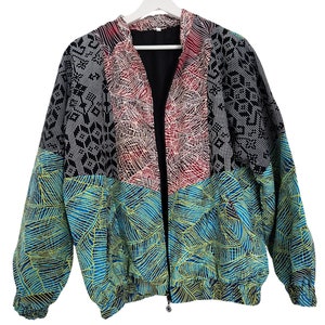 May include: A colorful zip-up jacket with a unique patchwork design. The jacket features a combination of patterns, including geometric shapes, leaf motifs, and abstract designs in black, red, blue, and white. The jacket is hanging on a white hanger.
