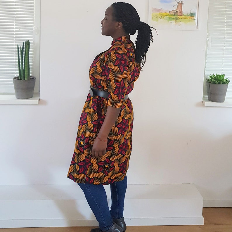 May include: A long, yellow, red, and black patterned dress with a black belt. The dress has a high neckline and three-quarter sleeves.