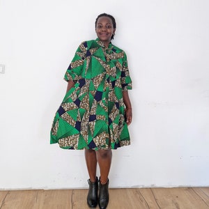 Könnte beinhalten: Eine Frau trägt ein grünes und schwarzes Kleid mit geometrischem Muster, einem Knopfkragenshirt und 3/4 Ärmeln. Sie trägt schwarze Stiefeletten.