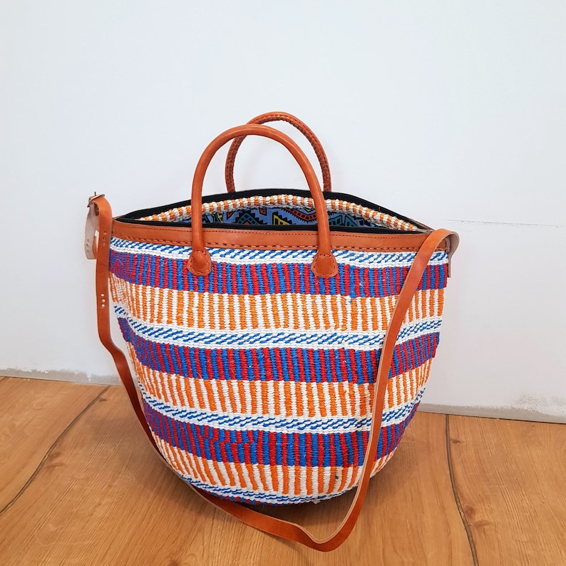 May include: A large, woven tote bag with a striped pattern in orange, blue, and white. The bag has brown leather handles and a brown leather strap.