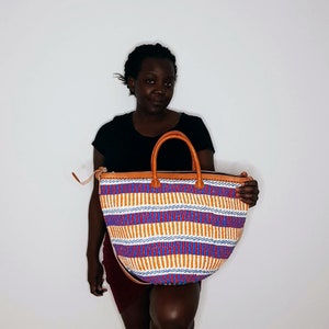 May include: A large, colorful tote bag with a woven design in shades of orange, blue, red, and white. The bag has a brown leather handle and a zipper closure.