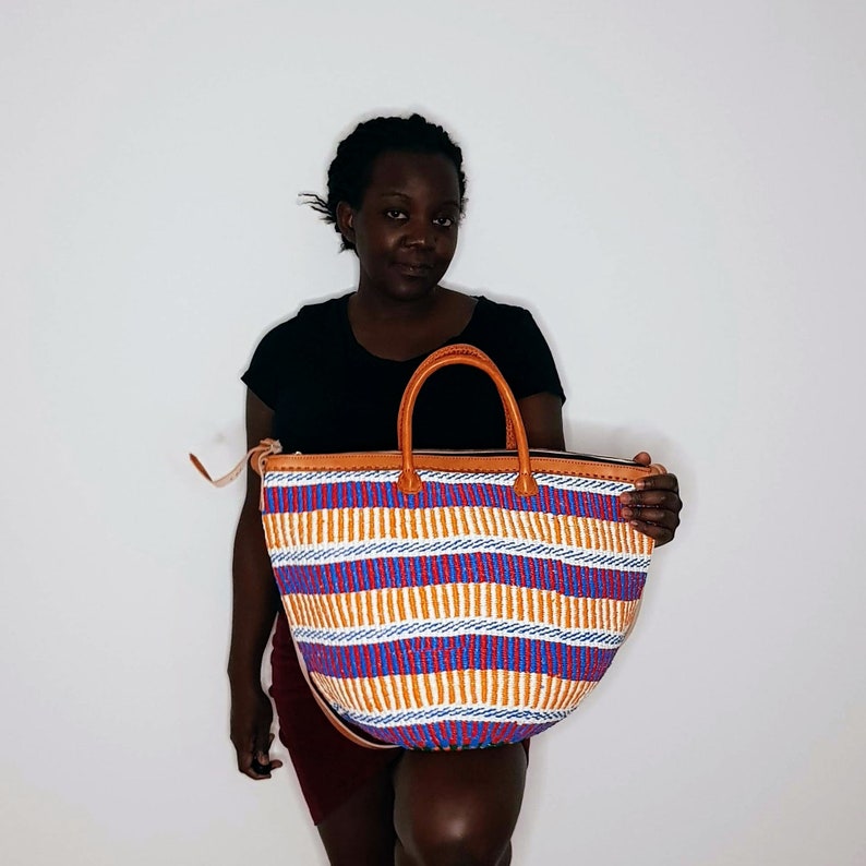 May include: A large, colorful tote bag with a woven design in shades of orange, blue, red, and white. The bag has a brown leather handle and a zipper closure.