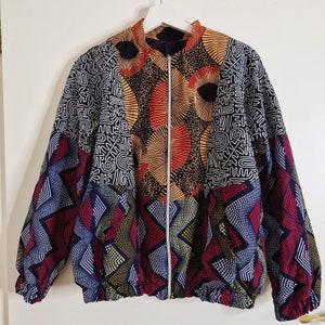 May include: A colorful patterned jacket with a zipper closure. The jacket features a variety of geometric and abstract designs in shades of red, orange, yellow, blue, and black.