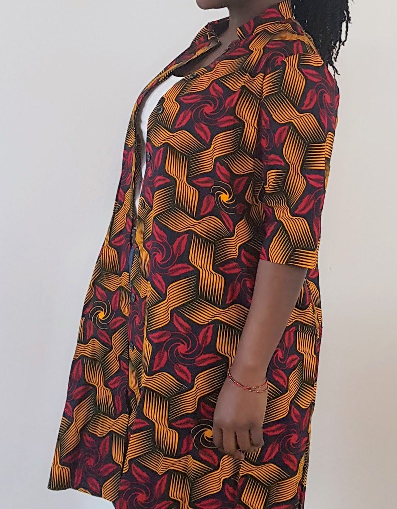May include: A long-sleeved button-up shirt with a geometric pattern in shades of red, orange, and black. The shirt has a mandarin collar and a relaxed fit.