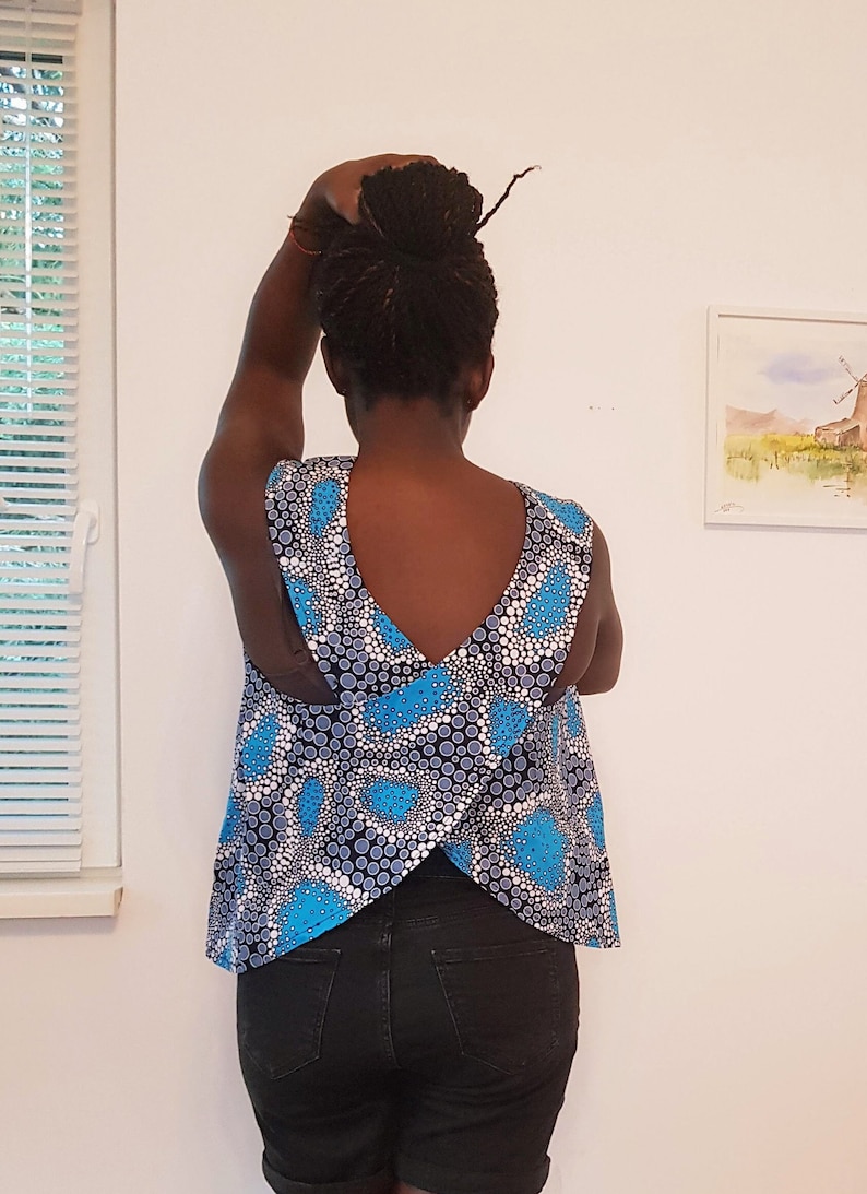 May include: A blue and white patterned sleeveless top with a criss-cross back design. The top is worn over black denim shorts.