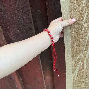 May include: Red beaded bracelet with small blue and white evil eye charms. The bracelet has a red string tie closure.