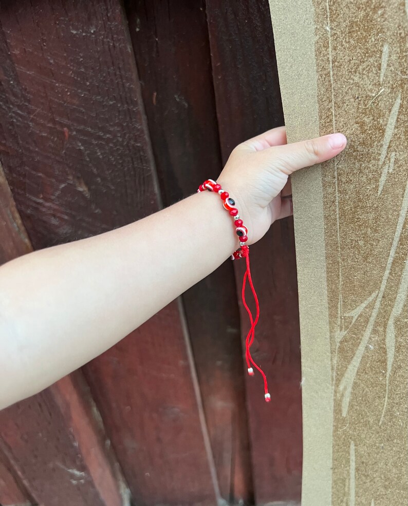 May include: Red beaded bracelet with small blue and white evil eye charms. The bracelet has a red string tie closure.