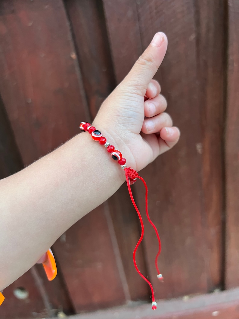 May include: Red string bracelet with small red and black evil eye beads and silver beads. The bracelet has a red string tie closure.
