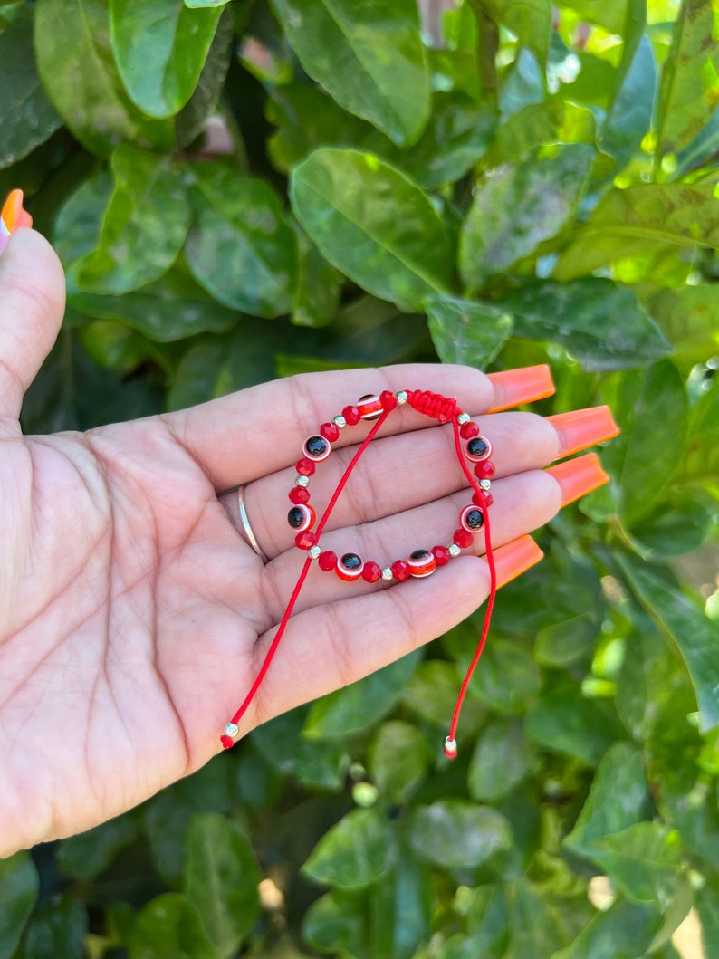 May include: Red string bracelet with silver beads and small blue and white evil eye charms.