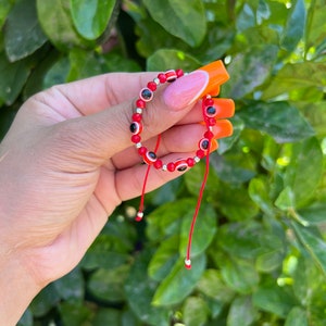 May include: Red string bracelet with silver beads and red evil eye charms.