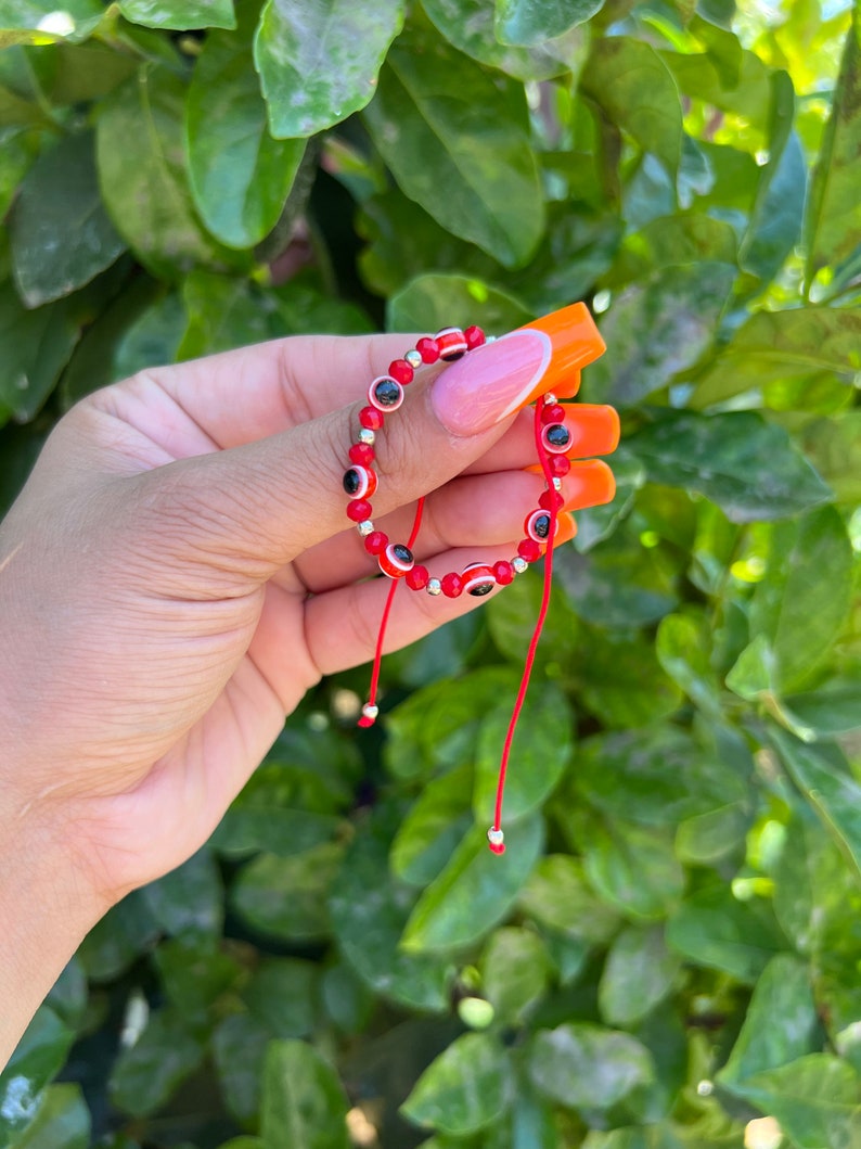 May include: Red string bracelet with silver beads and red evil eye charms.
