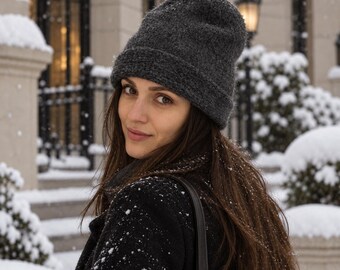 Puede incluir: Un gorro de punto en color gris carbón oscuro con un borde doblado. El gorro presenta una textura de hilo ligeramente difusa y se lleva puesto sobre la frente, cubriendo completamente la coronilla y las orejas con un estilo invernal clásico.