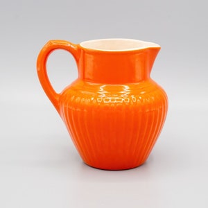 May include: A bright orange ceramic creamer with a white interior and a ribbed design.