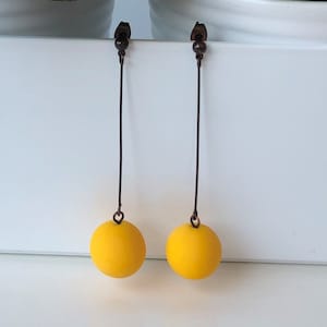Könnte beinhalten: Ein Paar lange gelbe Ohrringe mit einer runden Kugel am Ende jedes Ohrrings.