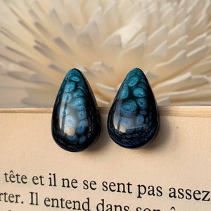 May include: A pair of teardrop-shaped earrings with a blue and black marbled design. The earrings are made of resin and have a glossy finish.